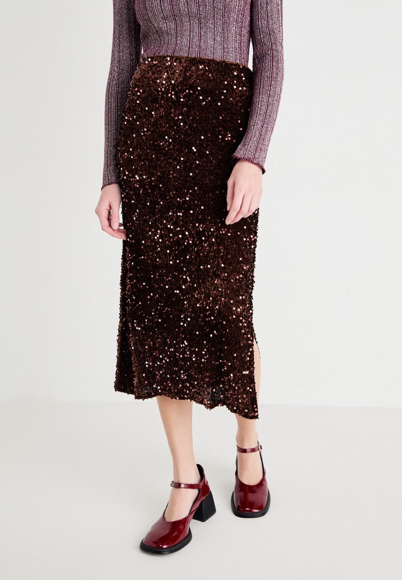 Jupe midi en sequins bruns avec fente latérale ; associée à des chaussures à talons blocs bourgogne brillantes. La texture semble réfléchissante et luxueuse.