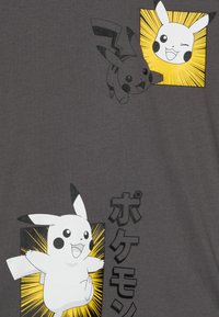 Grå T-skjorte med grafiske trykk av to Pikachu-karakterer i svart og hvitt, omgitt av gule eksplosjonsmønstre og japansk tekst.