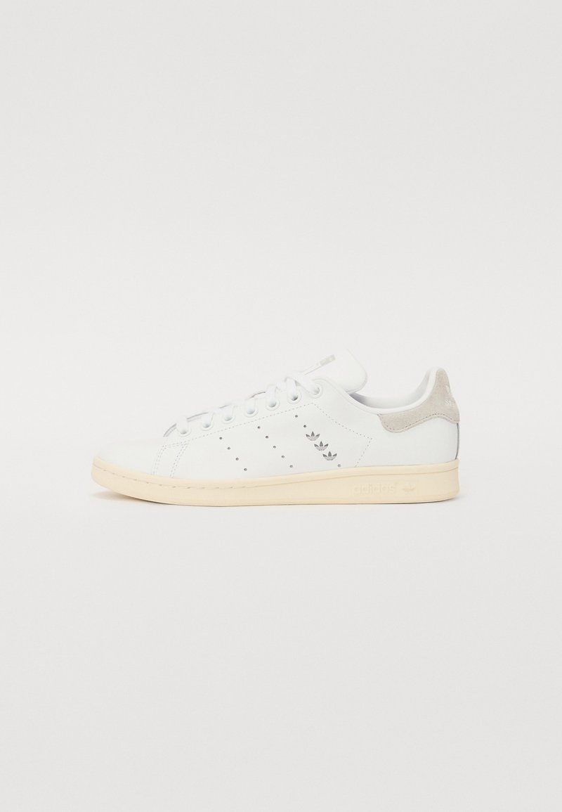 Fehér bőr sneaker világosszürke velúr sarokkal, perforált mintával és krémszínű gumitalppal. Az adidas logó a sarkán található.