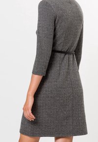 Robe en chevron gris avec des manches trois-quarts, une ceinture à la taille et un ourlet évasé. Le tissu semble texturé et structuré.