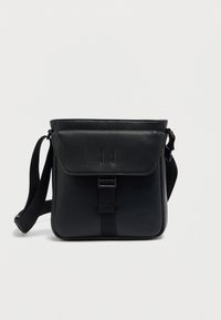 Μαύρο δερμάτινο τσαντάκι χιαστί με κλείσιμο με καπάκι, ρυθμιζόμενο λουράκι και ανάγλυφο λογότυπο. Λεπτή υφή και χαρακτηριστικά μινιμαλιστικού σχεδιασμού.