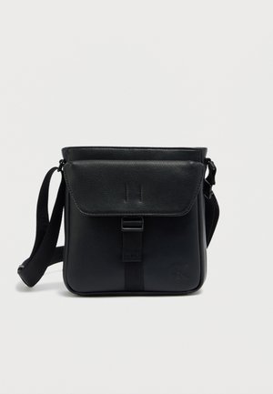 Μαύρο δερμάτινο τσαντάκι χιαστί με κλείσιμο με καπάκι, ρυθμιζόμενο λουράκι και ανάγλυφο λογότυπο. Λεπτή υφή και χαρακτηριστικά μινιμαλιστικού σχεδιασμού.