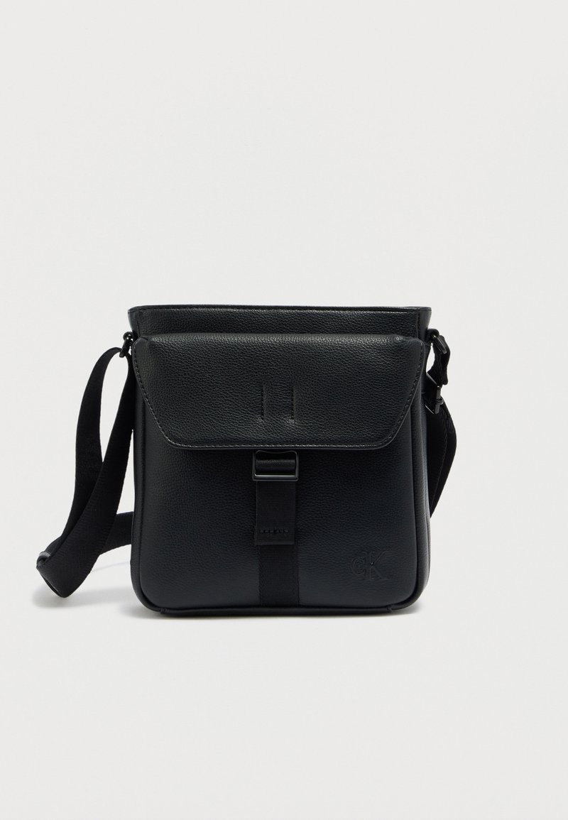 Μαύρο δερμάτινο τσαντάκι χιαστί με κλείσιμο με καπάκι, ρυθμιζόμενο λουράκι και ανάγλυφο λογότυπο. Λεπτή υφή και χαρακτηριστικά μινιμαλιστικού σχεδιασμού.