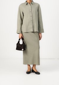 Chemise en lin vert clair à boutons, jupe assortie, chaussures plates noires et petit sac à main noir avec un accent blanc. Design simple avec une coupe décontractée.