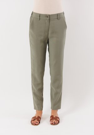 I pantaloni khaki presentano una vestibilità su misura, due tasche laterali e una chiusura con bottone frontale. Abbinati a sandali marroni con cinturini.
