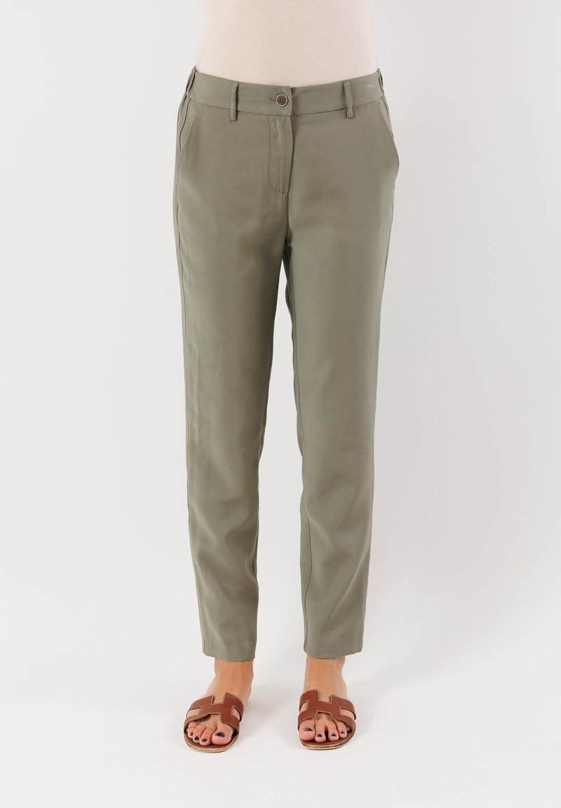 I pantaloni khaki presentano una vestibilità su misura, due tasche laterali e una chiusura con bottone frontale. Abbinati a sandali marroni con cinturini.