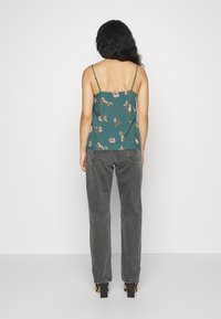 Camisola floral color teal con tirantes finos, combinada con vaqueros grises de cintura alta. El conjunto presenta un ajuste relajado y un diseño minimalista.