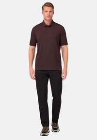 Burgundy pikétröja med krage, kort ärm och framknäppning med tre knappar, kombinerad med svarta byxor och grå sneakers. Slät tygkvalitet.