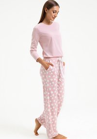 Różowa bluzka z długim rękawem w połączeniu z różowymi spodniami piżamowymi w duże białe kropki. Miękki, lekki materiał z kieszeniami i sznurkiem w talii.