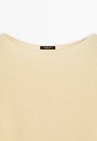 Cremfarbener Strickpullover mit weitem Ausschnitt und schwarzem Etikett mit der Aufschrift "Massimo Dutti Made in China" am inneren Kragen.