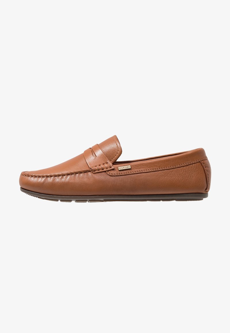 Mocassins en cuir marron avec un détail cousu sur le dessus, finition lisse, bout arrondi et semelle en caoutchouc. Accent de marque subtil visible.