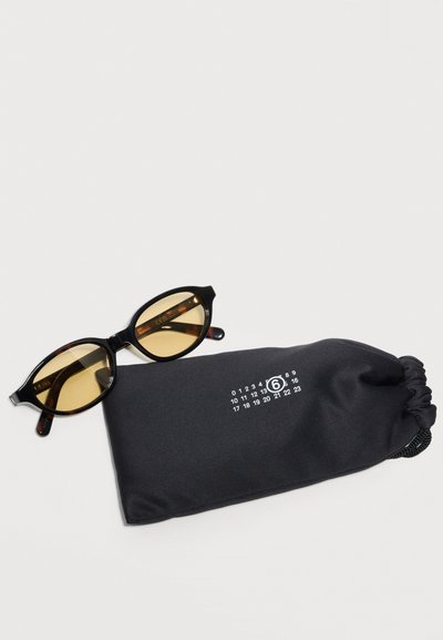 Black oval-framed sunglasses with amber lenses resting beside a black soft pouch featuring white printed numbers and a circled 6.