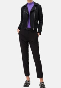Giacca da moto in suede nera sopra un dolcevita viola, abbinata a pantaloni neri a gamba affusolata e mocassini neri lucidi.