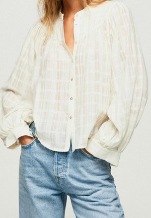 Hvid gennemsigtig bluse med ternet mønster, rund halsudskæring, knappedetaljer og pufærmer, kombineret med lyseblå denimjeans.