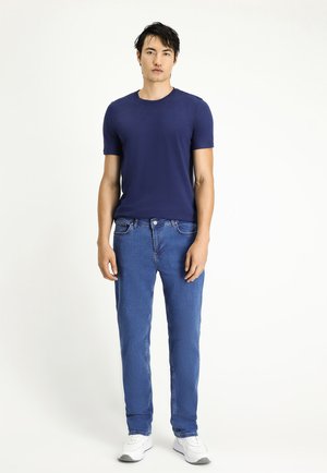 Camiseta ajustada de color azul marino con mangas cortas, combinada con jeans rectos de color azul claro. Zapatillas blancas completan el conjunto.