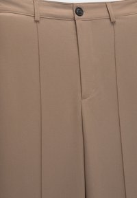 Beige op maat gemaakte broeken met een gladde textuur, voorzien van een enkele knoopsluiting, plooien en een subtiele stikselafwerking.