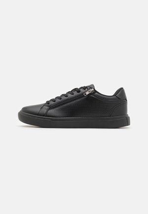 Baskets noires en matériau synthétique lisse, avec des détails perforés, un bout arrondi et une fermeture éclair latérale pour un accès facile.
