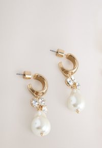 Gold hoop earrings feature a cluster of clear crystals and a white teardrop pearl hanging from the bottom. Smooth, glossy finish.
