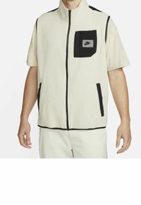 Chaleco de forro polar con cremallera en color crema y detalles en negro. Cuenta con un cuello alto, cremallera frontal y un bolsillo en el pecho izquierdo con el logo de Nike. Material Dry-fit.