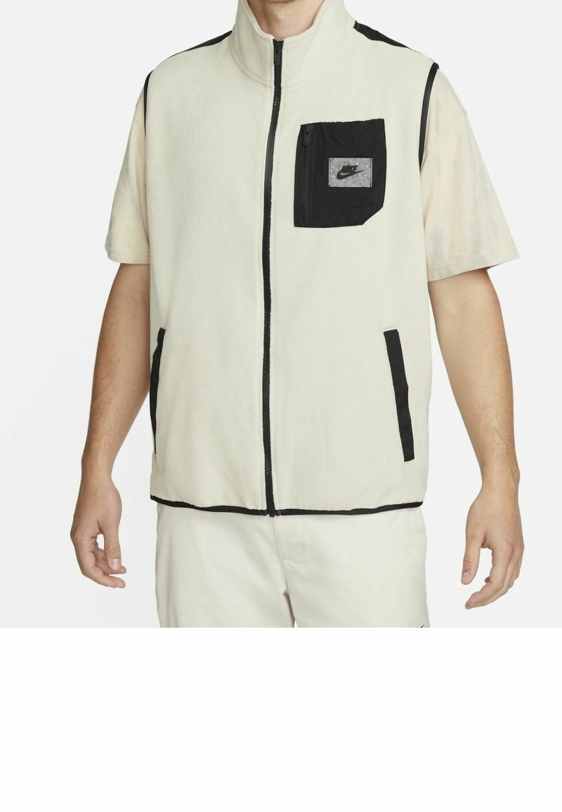 Chaleco de forro polar con cremallera en color crema y detalles en negro. Cuenta con un cuello alto, cremallera frontal y un bolsillo en el pecho izquierdo con el logo de Nike. Material Dry-fit.
