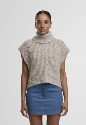 Beige, ribbed knit turtleneck poncho, short sleeves, with a high collar, worn over a blue denim mini skirt. Hem is slightly uneven.