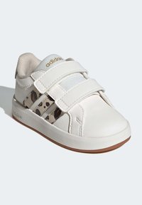 Scarpa sportiva bianca con due cinturini in Velcro, tomaia testurizzata e dettagli laterali con stampa leopardata marrone. Suola in gomma con leggero battistrada marrone.