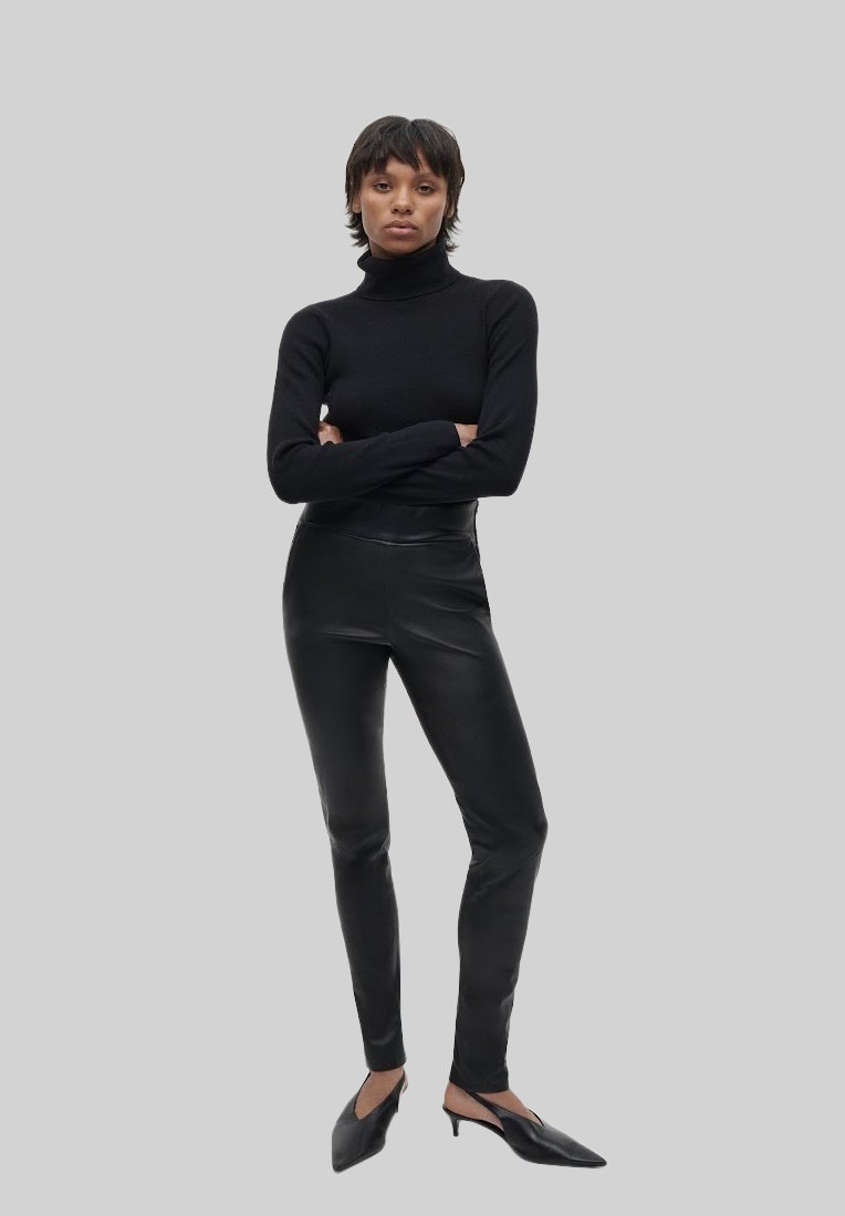 Schwarzer Rollkragenpullover kombiniert mit schwarzen Lederleggings und schwarzen spitzen Mules, die einen monochromatischen Look mit eleganten Texturen kreieren.