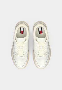 Weiße Ledersneaker mit durchbrochenen Details, cremefarbenen Schnürsenkeln und einer beigen Sohle. Enthält eine markierte Zunge mit roten, weißen und blauen Akzenten.