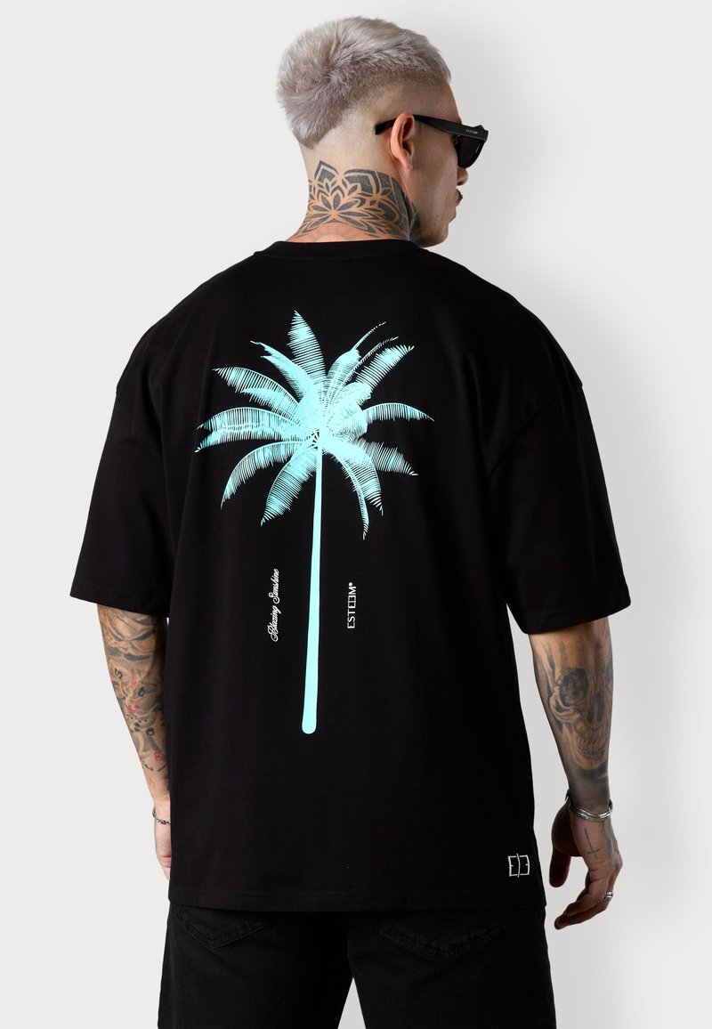 T-shirt noir oversize avec un graphique de palmier bleu clair au dos et des accents de texte. Manches courtes et tissu en coton lisse.