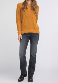 Sininen villapaita, jossa on teksturoitu kuvio, pyöreä pääntie ja ribattu hihansuu, yhdistettynä tummiin harmaisiin farkkuihin ja mustiin nilkkabootseihin.