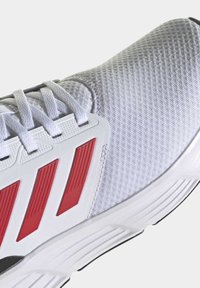 Basket sneaker avec une tige en mesh blanc respirant, des accents en caoutchouc rouge et des lacets texturés. Dispose d'une semelle intermédiaire blanche rembourrée et d'une semelle extérieure noire.