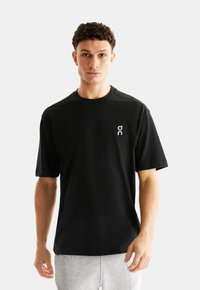 T-shirt noir à manches courtes en tissu doux avec un petit logo sur la poitrine. Encolure ronde simple et coupe décontractée.