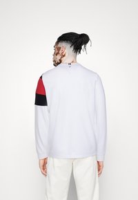 Langärmliger weißer Pullover mit roten und schwarzen Akzenten an den Ärmeln. Verfügt über einen runden Halsausschnitt und gerippte Bündchen. Lässige Passform.