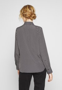 Blusa con motivo in bianco e nero caratterizzata da un design circolare, maniche lunghe e colletto. Il materiale sembra liscio con una vestibilità comoda.