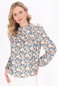 Blomstret bluse med flæset halsudskæring, lange ærmer og et mønster af blå, ferskenfarvede og cremefarvede blomster på lys baggrund.