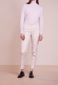 Jasnoróżowy sweter z długim rękawem i golfem w połączeniu z kremowymi spodniami w kant oraz czarnymi butami na sznurówki z ćwiekami.