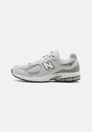 Zapatilla deportiva gris con parte superior de malla y sintético, que presenta un distintivo logo "N" reflectante, un collar acolchado y una suela amortiguada.