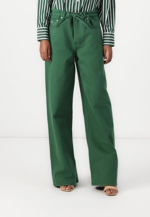 Pantalones de pierna ancha verdes, hechos de una tela resistente, con una cintura alta, presillas para cinturón, bolsillos frontales y un logo de la marca visible en la cadera.