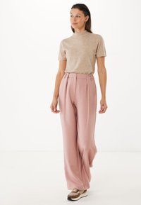 Beige krátký rukáv top spárovaný s světle růžovými kalhotami s vysokým pasem, které mají záhyby a volný střih, doplněný béžovými a hnědými teniskami.