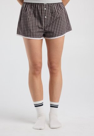 Persoon draagt zwart-witte geruite korte broek met knopen en witte sokken met twee zwarte strepen, staand op een effen achtergrond.