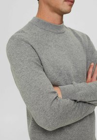 Šedý pletený svetr s texturovaným vzorem, kulatým výstřihem a žebrovanými manžetami. Tkanina vypadá měkce a teple, s přiléhavým střihem.