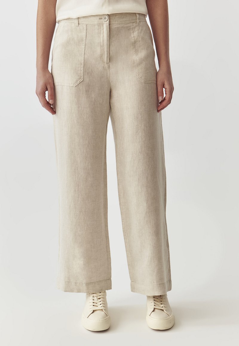 Beige linnen wijde pantalon met twee voorzakken, sluiting met een knoop aan de voorkant en een relaxte fit. Gekleed met witte veterschoenen.