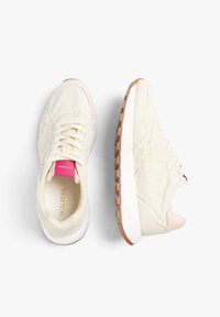 Sneakers color beige chiaro realizzati in canvas con una parte superiore testurizzata, suola intermedia bianca e suola esterna in gomma marrone. Presenta un'etichetta rosa sul tallone.