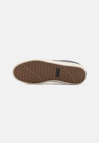 Shoe sole features a rubber material with a textured brown pattern. The edge is cream-colored, highlighting the contrast with the sole design.