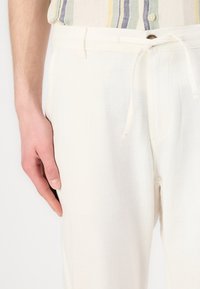 Vita linnbyxor med snörning i midjan, med framfickor och en slät, texturerad yta. Pairad med en randig skjorta.