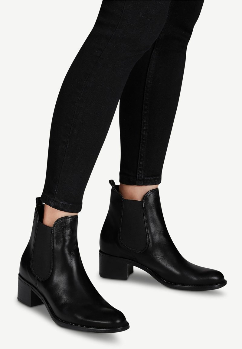 Bottes courtes en cuir noir avec talons blocs bas portées avec un pantalon noir ajusté.