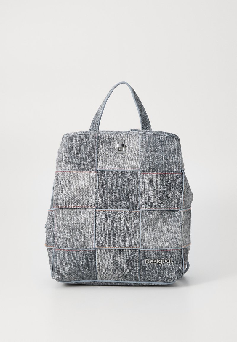 Denim patchwork backpack with a textured finish, featuring blue stitching and a silver hardware clasp. Embroidered "Desigual" logo on front.