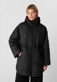 Schwarz gesteppte Daunenjacke mit Kapuze, Kordelzug in der Taille und Reißverschluss. Mit großen aufgesetzten Taschen und lockerer Passform. Glatte Textur.