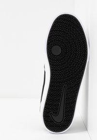 Semelle de chaussure en caoutchouc noir avec un motif en zigzag et un grand logo swoosh. Détail de bord blanc le long des côtés.