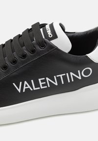 Crne kožne tenisice s bijelim detaljima, s debelim potplatom, okruglim vrhom i istaknutim "VALENTINO" logom sa strane.
